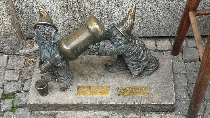A statue of two dwarves with beards and pointy hats pouring alcohol from a bottle