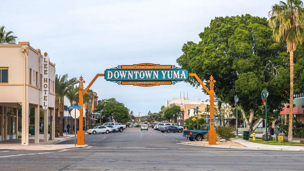 An orange and green sign that says "Downtown Yuma" on a tree-lined street