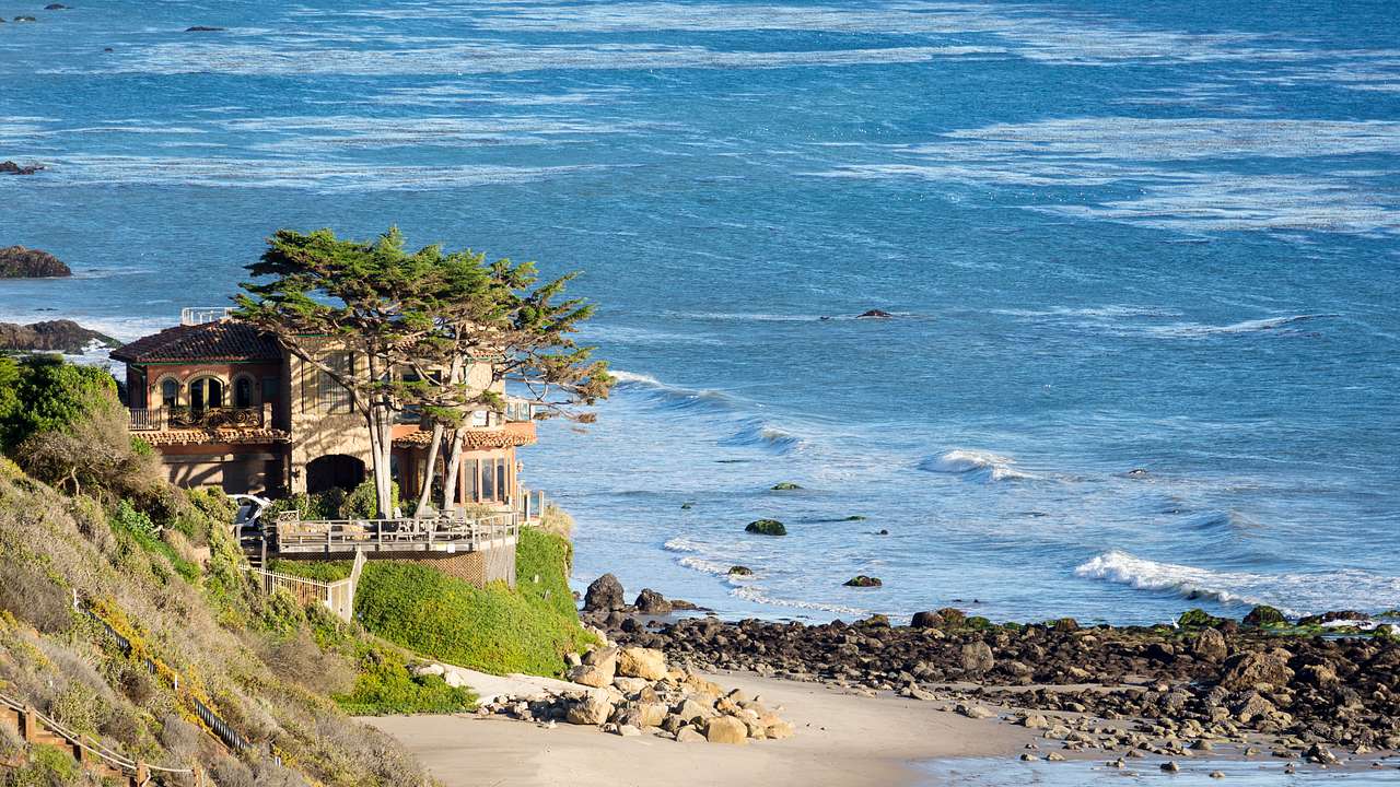 Beach mansion with trees overlooking the ocean and a rocky beach