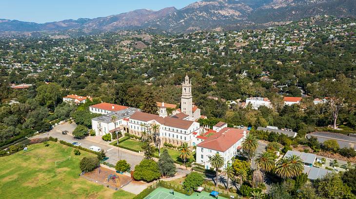 Aerial view of a Spanish church with houses, trees, and mountains in the background