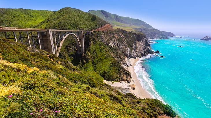 A bridge between green mountains overlooking the turquoise ocean on a sunny day