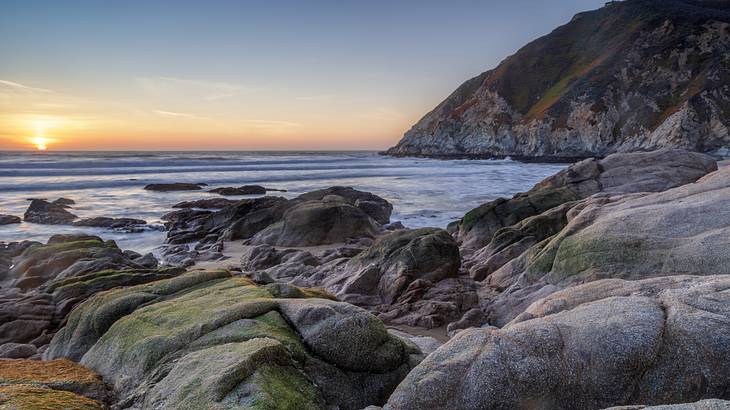 Sunset by a rocky coastline with a hill in the background