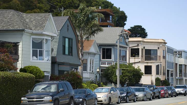 Cars parked in front of homes with green trees and blue sky behind