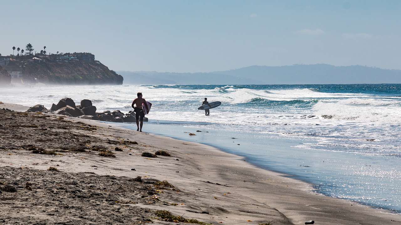 Two surfers on a sandy beach with waves, on a windy and sunny day
