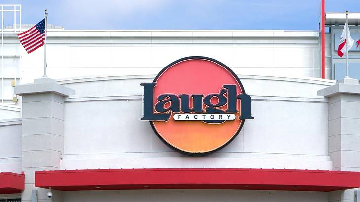 A white building with red awning, flags, and a "Laugh Factory" sign