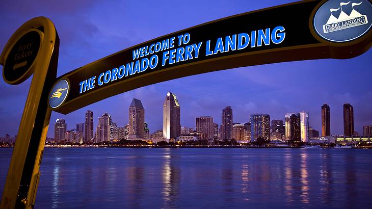 Signage with "Welcome to the Coronado Ferry Landing" and skyline reflecting on water