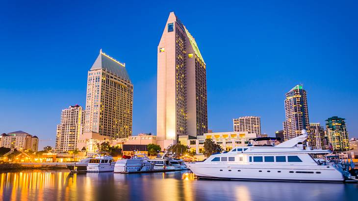 Yachts docked in a pier with lit skyscrapers reflecting on water at night