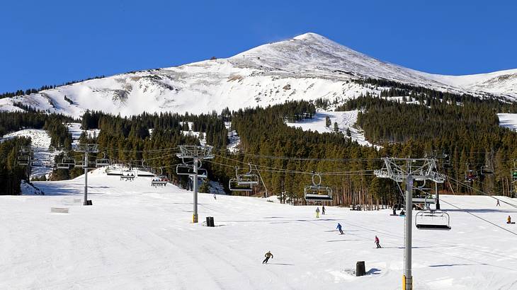 People skiing and a gondola at the foot of a snow-covered mountain in winter People skiing and a gondola at the foot of a snow-covered mountain in winter