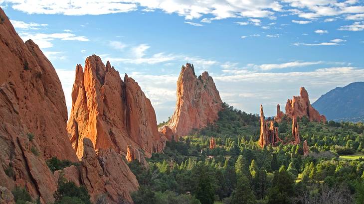 Red rock mountains surrounded by green trees under a blue sky with some cloud Red rock mountains surrounded by green trees under a blue sky with some cloud