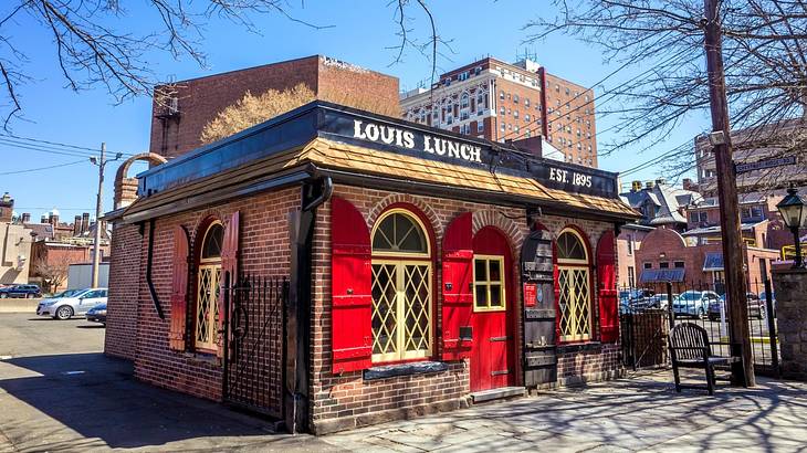 A red brick restaurant with a red door and a sign that reads "Louis Lunch" A red brick restaurant with a red door and a sign that reads "Louis Lunch"