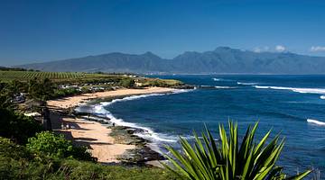 View of a sandy coastline with blue ocean surrounded by greenery and mountains