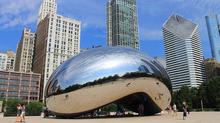 A huge metal bean sculpture against tall modern buildings under a partly cloudy sky