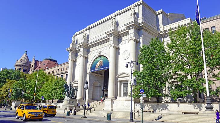 A white museum building with trees on either side and yellow taxis in front