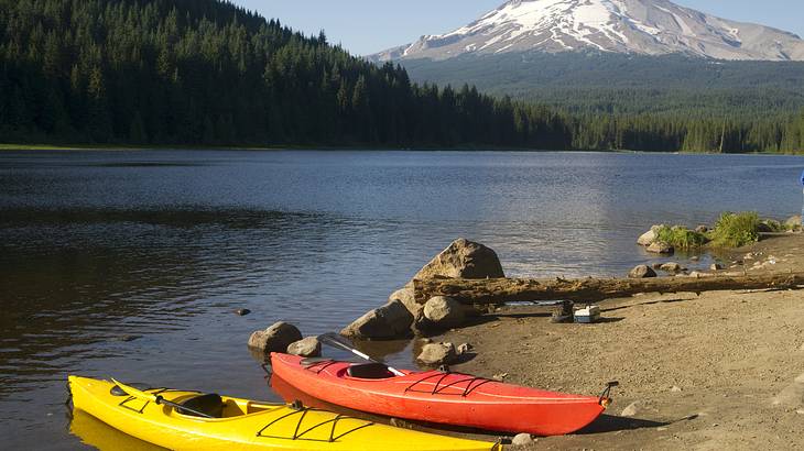Two kayaks on the shore of a lake with a forest and snow-covered mountain behind