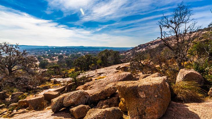 Huge boulders on a hill with bare trees under a partly cloudy blue sky