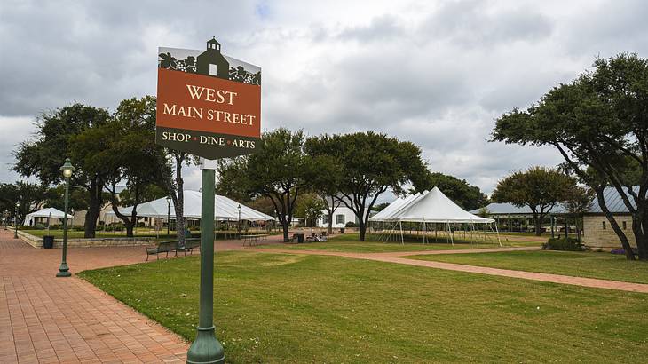 "West Main Street" signage in a park with trees on a cloudy day