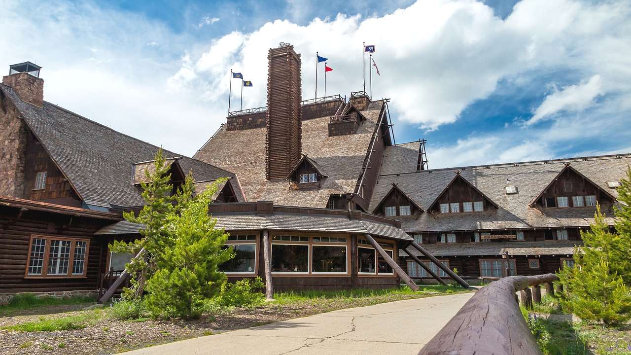 A lodge-style hotel with wooden walls and flags on the roof next to a path and trees
