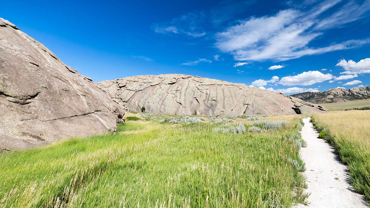 Some large boulders next to a small path and green grass under a blue sky