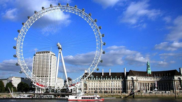 Riverside view of the London Eye and passing river cruise boat on a sunny day