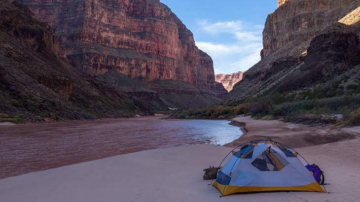 A blue tent on the sand overlooking a river and the canyon