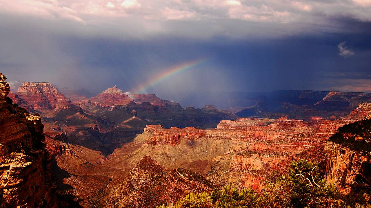 A rainbow over a canyon with a dark sky and clouds