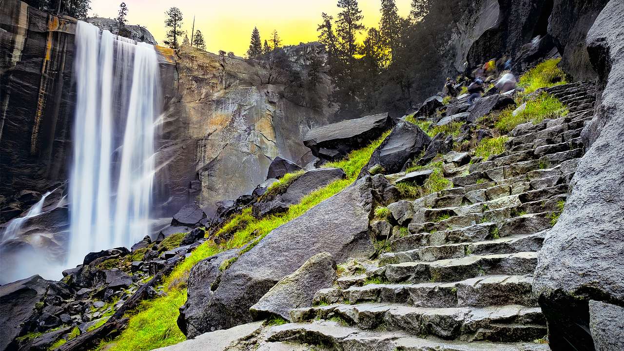A waterfall and a rocky cliff with trees in the distance