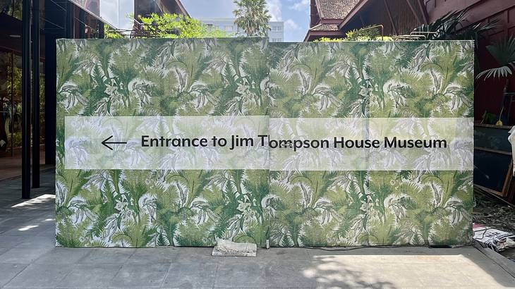 A green and white board that says "Entrance to Jim Thompson House Museum"