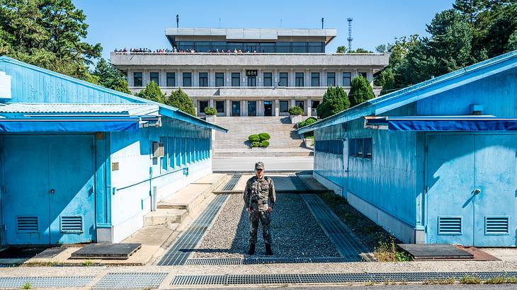 Two small blue buildings with a soldier standing between them