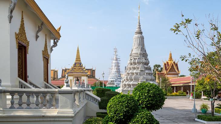 A tall tower-like temple next to another building, trees, and a green bush