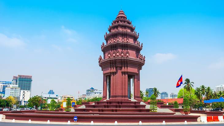 A tower-like monument on a pedestal surrounded by a road and trees