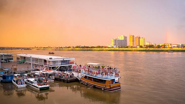 Boats on a river with some city buildings on the shore at sunset