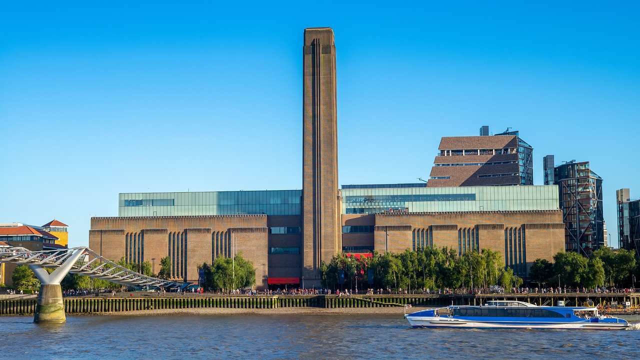 An industrial-style building with a tall tower, next to a river under a blue sky