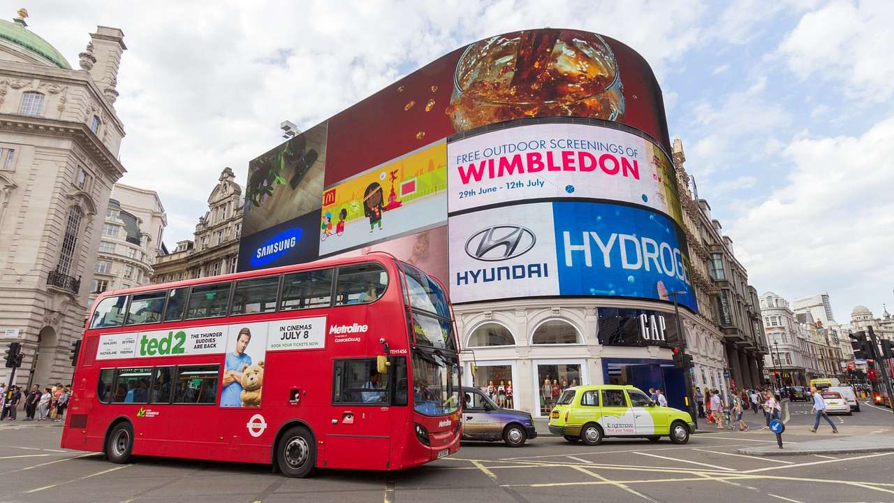A building with digital billboards on it, next to a road with a red bus and cars