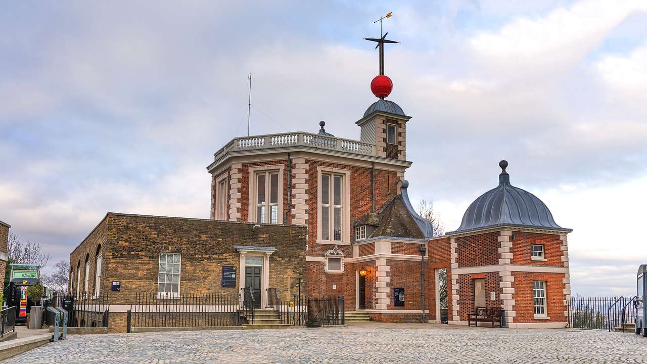 A red brick building with a weather vane atop it on a cloudy day