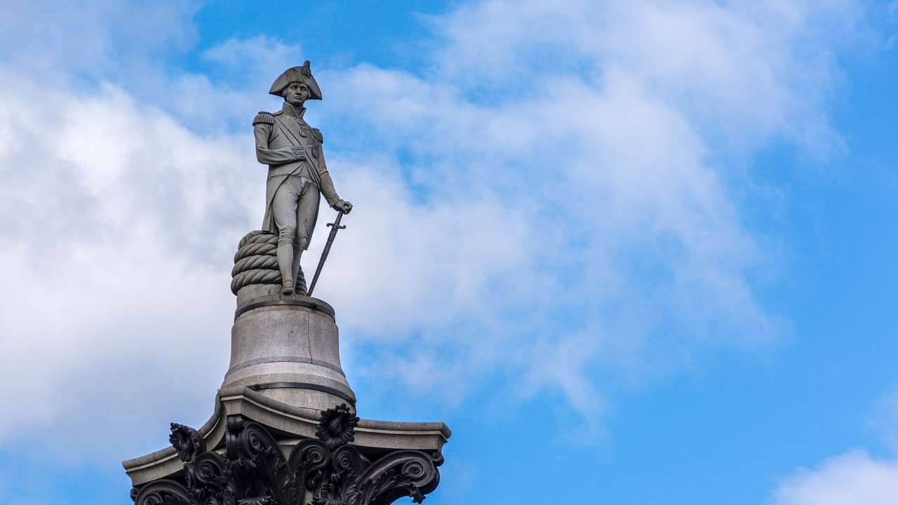 A statue of a man leaning on a sword, next to a blue sky with clouds