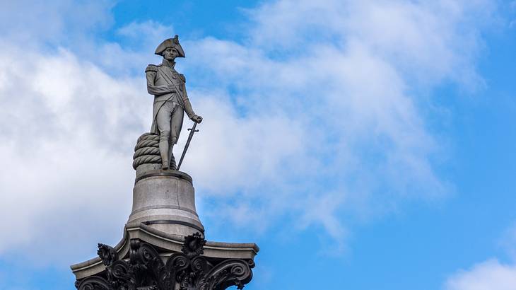 A statue of a man leaning on a sword, next to a blue sky with clouds