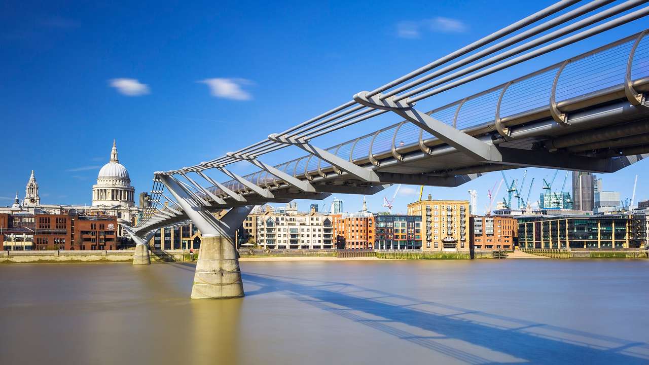 A pedestrian bridge over water, leading to historic buildings on the riverbank