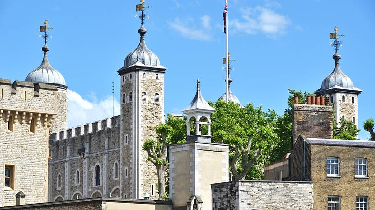 A gray stone building with spires having a flag on top of each under a sunny day