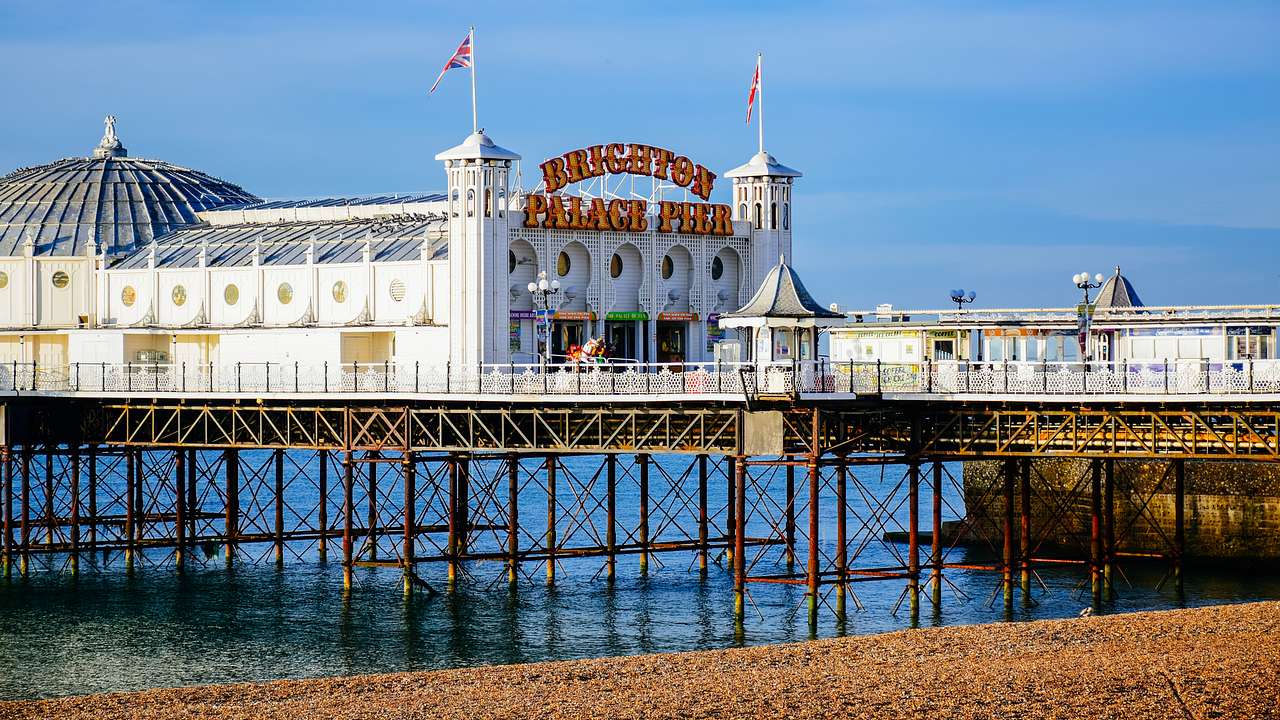 A pier over water and sand in front of a domed white building on a sunny day