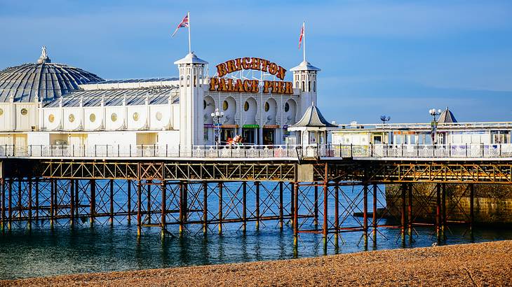 A pier over water and sand in front of a domed white building on a sunny day