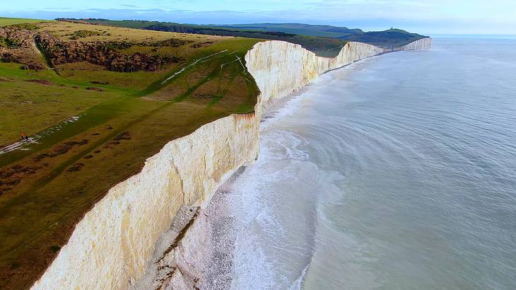A stretch of white cliffs with grassy meadows on top, surrounded by water