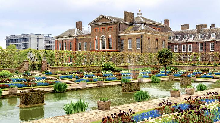 A grand brick palace with a garden full of flowers and a pond in front