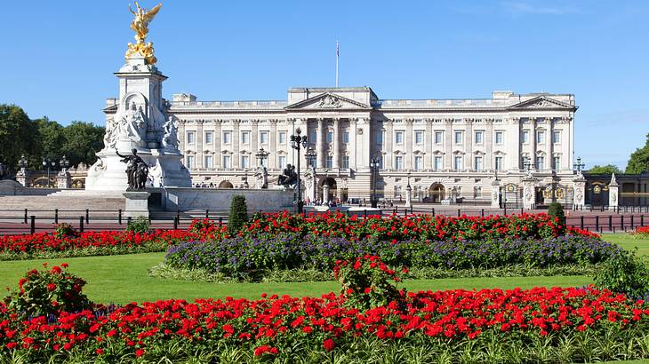 A massive palace with a golden statue facing red flowers and grass under blue skies