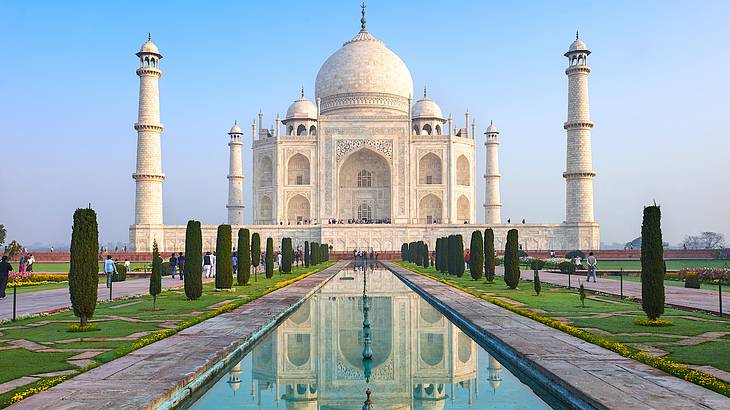 A huge India landmark made of white marble, facing a garden and a pond on a clear day