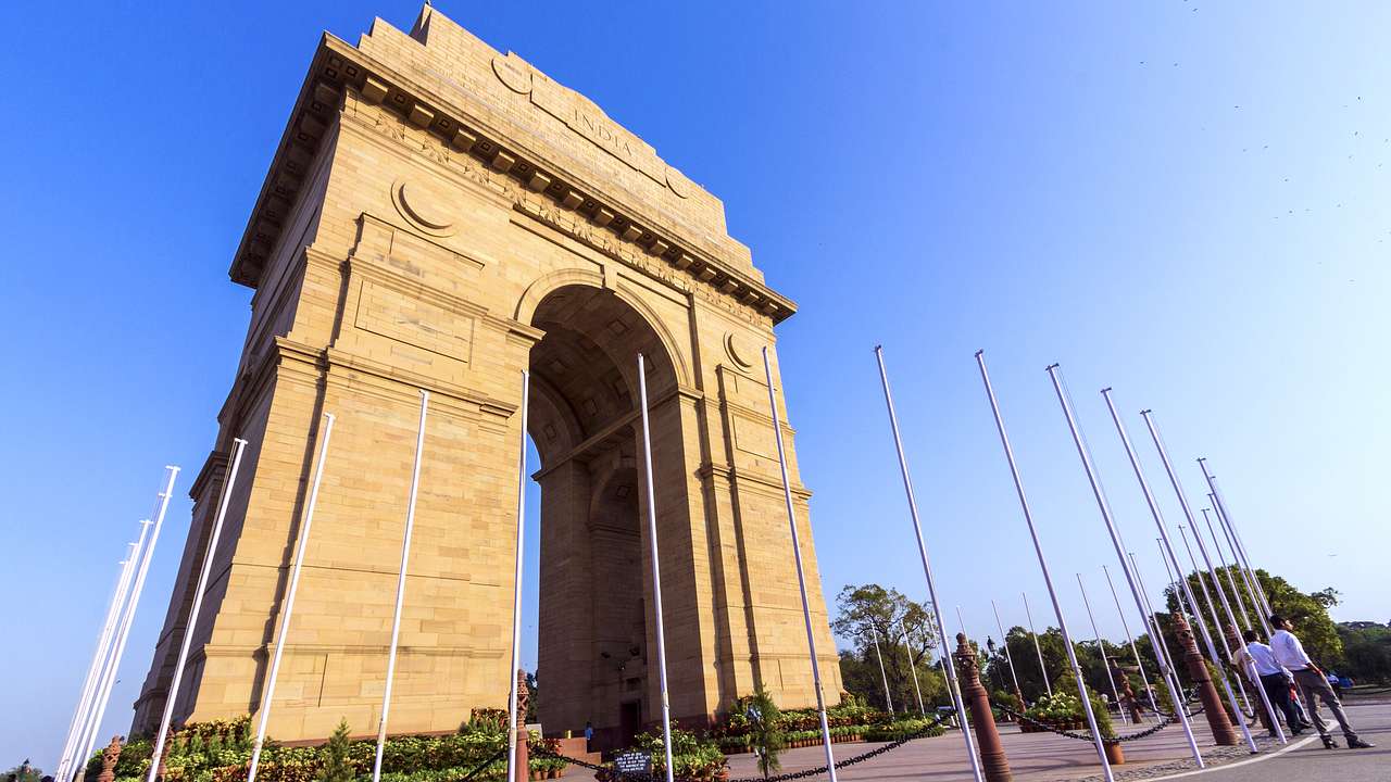 A huge monumental stone gate surrounded by thin metal posts against a clear blue sky