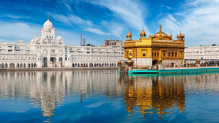 A golden temple floating on a body of water with a massive white building on the left