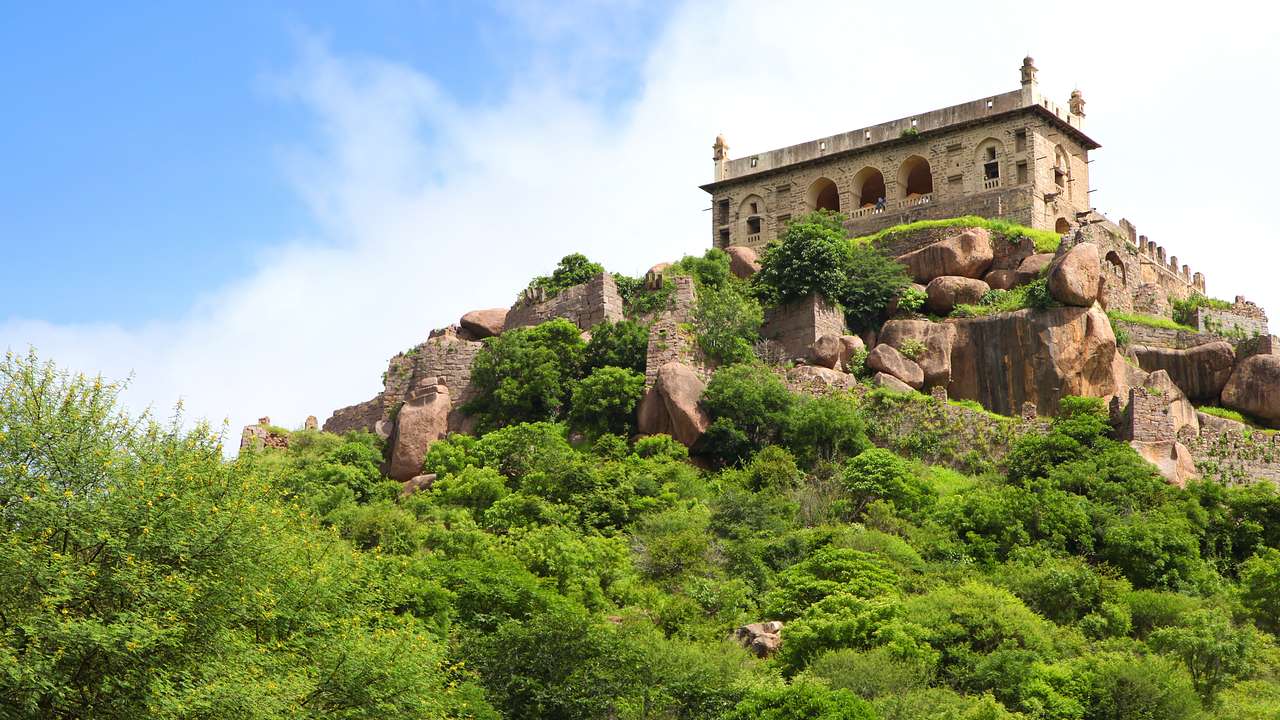 A building surrounded by big rocks on a cliff covered with trees and greenery