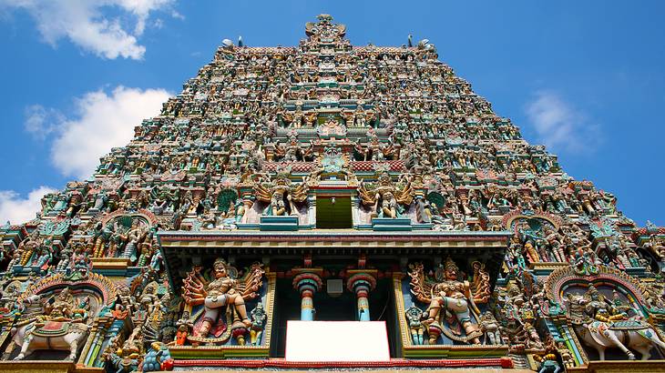 The exterior of a tower-like temple from below covered in colorful statues