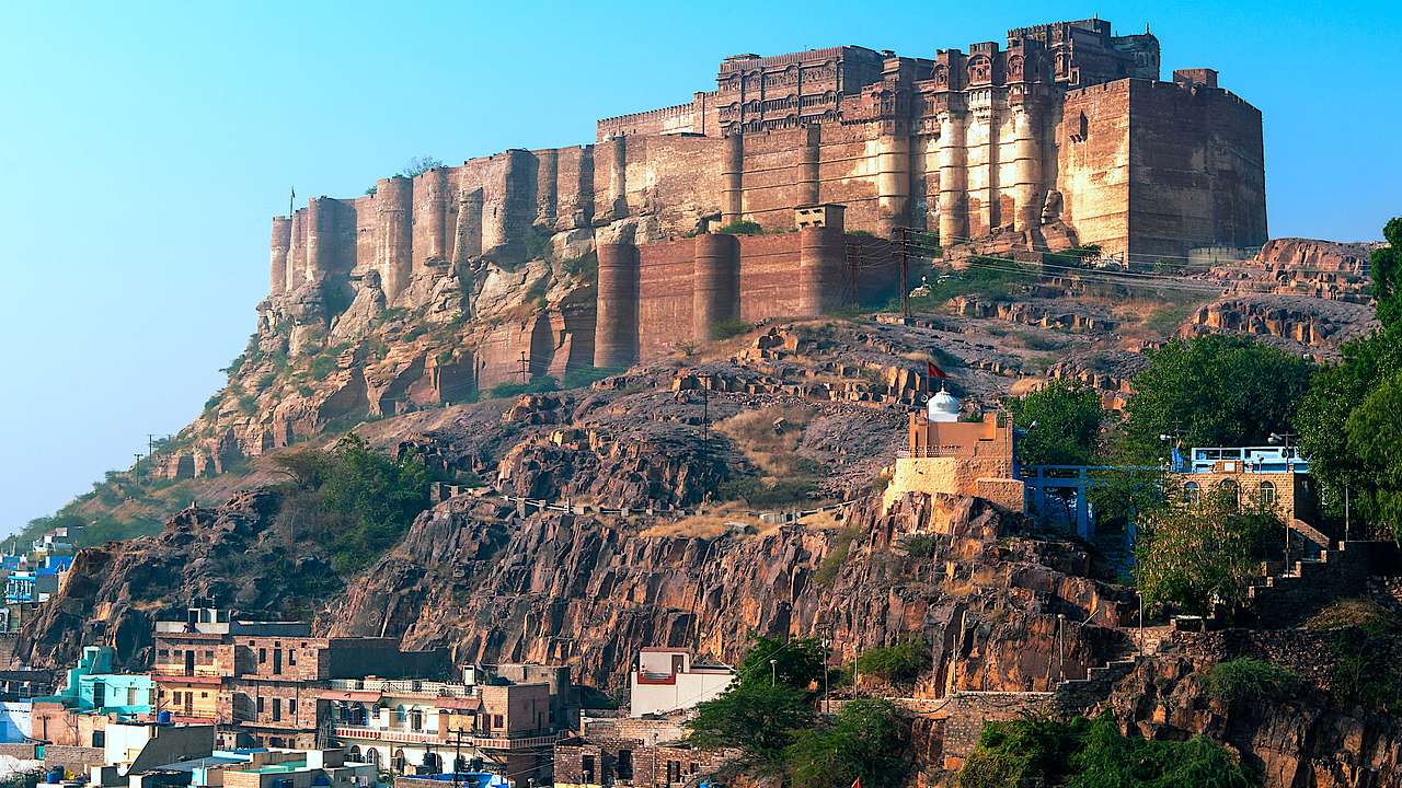 A massive fort palace on a hill in India overlooking buildings under a clear blue sky
