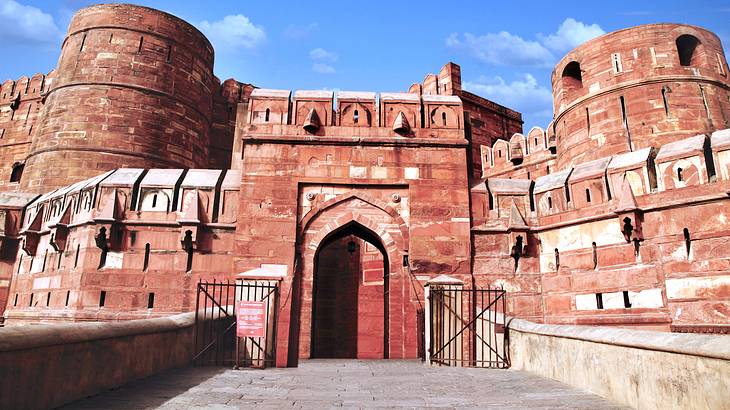 The view outside a gate and two towers of a red sandstone fort complex on a sunny day